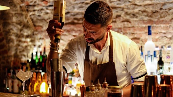 Een professionele bartender schenkt geconcentreerd een drankje in een cocktailshaker.